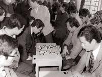교수 바둑대회 (1975), 바둑판을 사이에 두고 경기를 하고 있으며 주변 인물들이 관람함