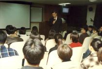 학생 활동 - 수업, 안경을 쓰고 검은 양복을 입고 있는 교수님의 앞모습과 앉아있는 학생들의 뒷모습