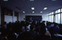 수업, 교수님이 칠판 앞에서 강의하고 있고 앉아있는 학생들의 뒷모습